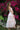 Teen girl wearing blush bloom pink two piece top and tiered maxi skirt with ruffle detaling standing in garden with flowers